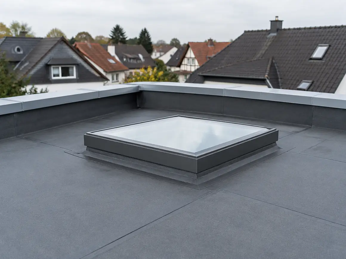 Neu abgedichtetes Flachdach mit Flachdachfenster, dahinter die Dächer einer Kleinstadt