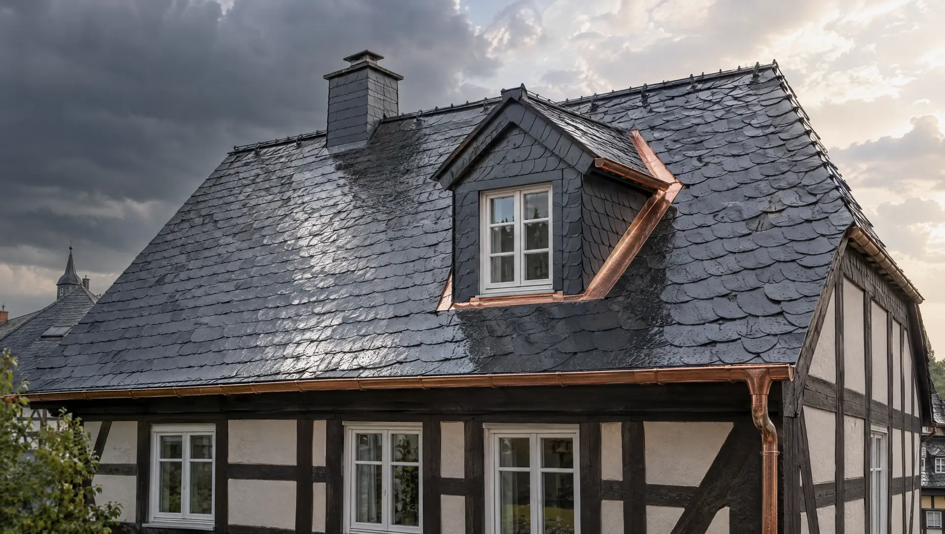 Fachwerkhaus mit frisch gedecktem Schieferdach in Altdeutscher Deckung nach einem Regenschauer; die Gaube ist neu in Schiefer eingedeckt, Kehle, Verwahrung und Dachrinne sind aus Kupfer, dahinter zieht der Sturm ab