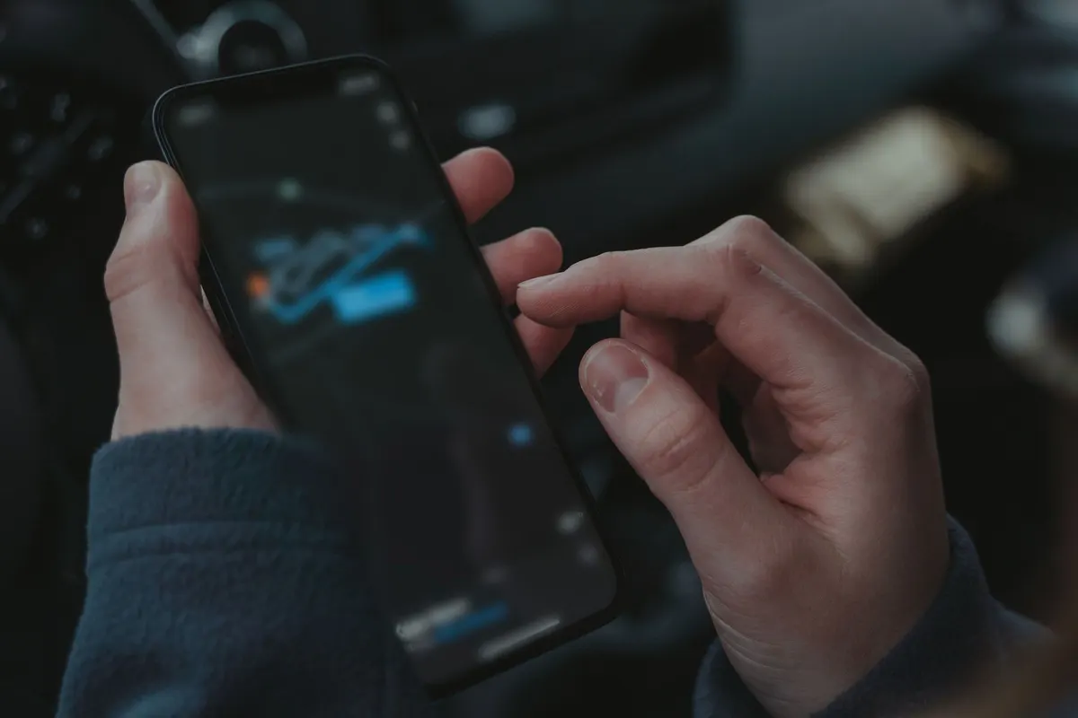 Zwei Hände bedienen ein Smartphone mit Navigationsroute im dunklen Innenraum eines Transporters.